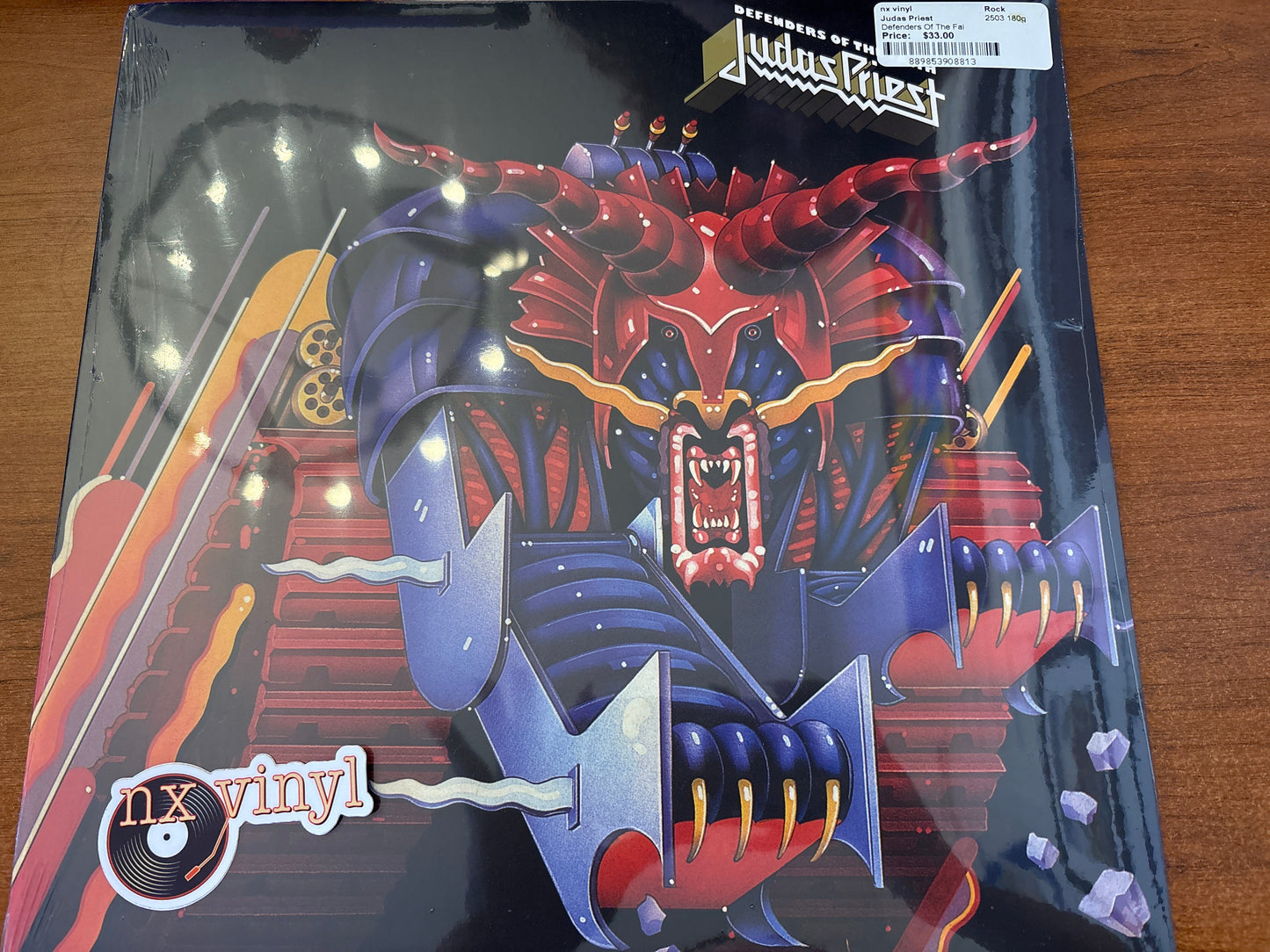 Vinyl record cover with a dragon design and 'Judas Priest' branding on a wooden surface.