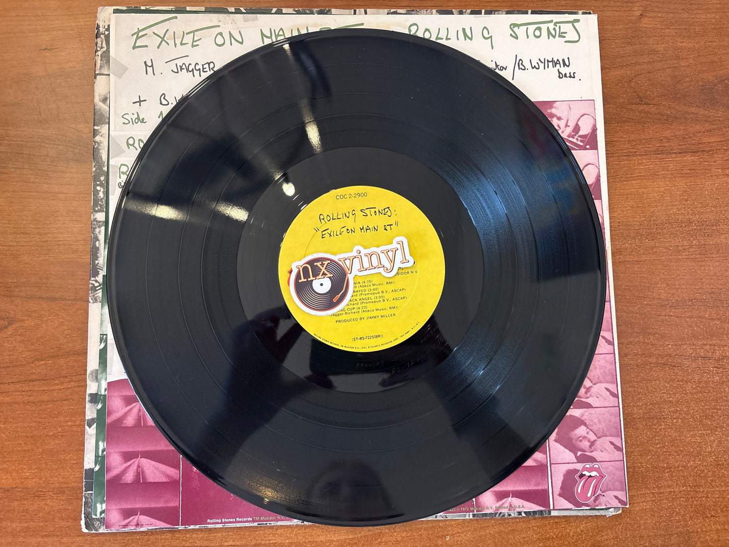 Vinyl record with a yellow label on a pink and white patterned sleeve, on a wooden surface.